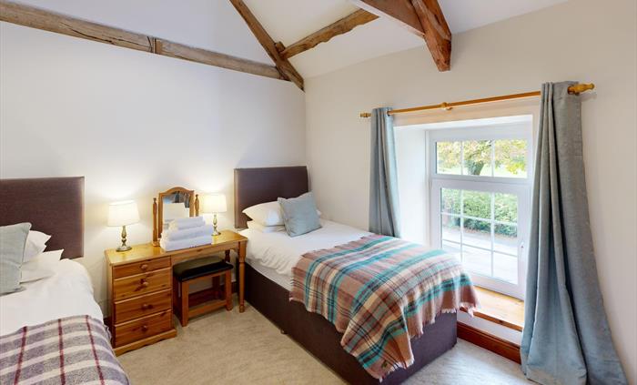 A twin bedroom with high vaulted ceilings and exposed beams, featuring two single beds with soft throws and a wooden dressing table between.